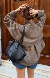 Chaqueta corta de corte recto con estampado de cuadros pequeños en tonos marrones y beige. Presenta cuello alto, mangas largas y cierre frontal oculto.