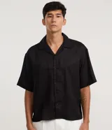 Camisa de lino blanca de corte boxy, manga corta, cuello bowling y cierre frontal de botones.