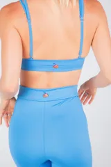 Top deportivo celeste con tiras regulables y desmontables para usarlo de tres formas distintas: con una tira cruzada detrás del cuello, con tiras rectas o tiras cruzadas por detrás.