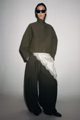 Chaqueta corta de tejido grueso color verde oliva, con cuello alto y cierre frontal completo de cremallera plateada. Presenta un corte amplio y mangas largas caídas.