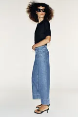 Jeans culotte de tiro alto, color azul, con pernera ancha, nervios marcados en el delantero y bolsillos de parche con botones metálicos. Cuenta con cierre frontal de cremallera y botón metálico.