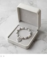 Pulsera elástica compuesta por una alternancia de perlas blancas y esferas metálicas plateadas.
