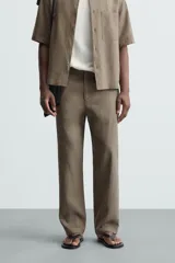 Pantalón de calce relajado confeccionado en tejido de viscosa y yute color tostado. Presenta cintura elástica ajustable con cordón, bolsillos laterales, bolsillos traseros de vivo y cierre frontal con cremallera y botón.