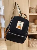 Mochila de nylon color negro con cierre frontal, correas ajustables estampadas con el nombre de la marca y parche bordado decorativo en el frente.