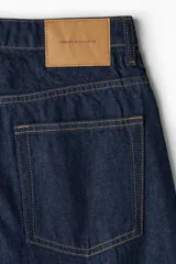 Jean de tiro alto con corte baggy, confeccionado en denim de algodón. Presenta diseño de cinco bolsillos, cierre frontal con botón y silueta de pierna curva con volumen en la cadera.