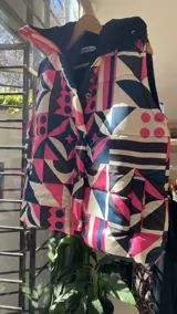 Chaleco marrón con estampado abstracto en tonos marrones y negros, con cierre frontal y broches a presión. Interior forrado con tela de peluche color crema y bolsillo interno.