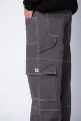 Pantalón tipo carpintero de corte relaxed fit y tiro medio, confeccionado en denim negro con costuras a contracolor en blanco. Presenta múltiples bolsillos cargo laterales, un bolsillo con cierre en la parte inferior y presillas utilitarias.