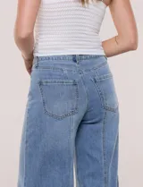 Pantalón jean de tiro alto con calce ajustado en la cadera y pierna de corte ancho tipo wide leg. Presenta costuras verticales en el frente y bolsillos aplicados.
