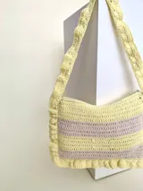 Cartera tipo shoulder bag tejida a crochet en hilo de algodón, con diseño a rayas en tonos de rojo y rosado, y detalles de volados en los bordes y la manija de hombro.