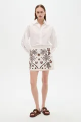 Minifalda de algodón blanca con bordado artesanal en tonos marrones que presenta un diseño de palmeras y flores.