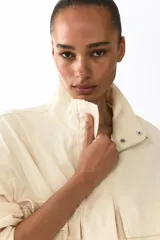 Campera corta de sarga con cuello elevado, solapa rompevientos con cierre y botones a presión ocultos. Diseño oversized con hombros caídos, bolsillos delanteros de fuelle con solapa y cordón elástico ajustable en el bajo.