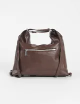 Cartera hobo convertible a mochila, color marrón, confeccionada en cuero sintético. Presenta un diseño con bolsillo frontal con solapa y cierre de hebilla metálica, además de correas ajustables y herrajes plateados.