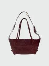 Bolso shoulder bag de Balmain en color bordó, confeccionado en cuero, con doble asa superior y correa ajustable para el hombro. Presenta costuras decorativas y el logo de la marca estampado en tono dorado en la parte frontal.