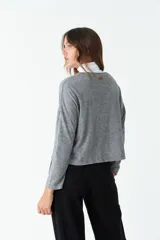 Cardigan de tejido de punto color gris melange, con escote en V, cierre frontal con botones y bolsillos tipo cartera. Presenta un diseño de corte recto y mangas largas.