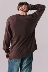 Remera de manga larga en color marrón Kahlúa, de corte holgado y cuello redondo. Presenta un estampado gráfico frontal de estilo vintage con el texto "NEW YORK", "19 75", "CHAMPIONS" y un emblema circular central.