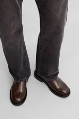 Bota tipo Chelsea de piel color marrón oscuro, con paneles elásticos laterales, tirador trasero y suela de goma con ligero tacón.