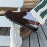 Zueco de cuero marrón con diseño cerrado en la parte delantera, suela track de goma y tira trasera ajustable con hebilla metálica.