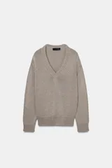 Sweater de punto grueso color beige, con cuello en V profundo y mangas largas. Cuenta con terminaciones acanaladas en el cuello, los puños y el ruedo.