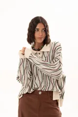 Buzo de tejido de punto con diseño de rayas verticales onduladas en tonos verde y marrón sobre base color crudo. Presenta cuello tipo polo con cierre frontal de botones y mangas largas con puños acanalados.