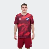 Remera deportiva Umbro modelo Press, de color rojo con un estampado abstracto en tonos más oscuros, cuello redondo y manga corta. Incluye el logo de la marca en el pecho y el escudo del Club Nacional de Football.