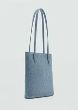 Bolso tipo tote de tamaño pequeño, confeccionado en piel bovina color azul con diseño troquelado de ojales metálicos en toda su superficie. Cuenta con doble asa de hombro y forro interior de poliéster.