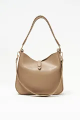 Cartera tipo hobo color beige, de diseño estructurado con cierre superior y una tira vertical con detalle de dije metálico circular en la parte frontal. Cuenta con asa corta trenzada y herrajes dorados.