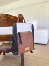 Mochila de cuero tricolor en tonos marrón tostado, negro y blanco, con bolsillo frontal con cierre, tiradores de cuero y detalle de etiqueta con logo grabado.