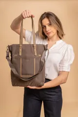 Bolso tipo tote bag de símil cuero color rosa pálido, con asas dobles y detalles de costura en color beige claro. Presenta un bolsillo frontal rectangular aplicado y herrajes metálicos.