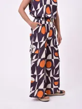 Pantalón ancho de tiro alto con elástico en la cintura y bolsillos cargo laterales. Presenta un estampado geométrico abstracto en tonos morado oscuro, blanco y naranja.