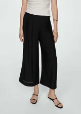 Pantalon wideleg negro de tejido fluido con diseño de tablas frontales y detalle de bordado en el ruedo. Cuenta con cierre delantero de cremallera y botón.