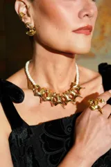 Collar de diseño orgánico compuesto por una hilera de perlas y una pieza frontal metálica dorada de formas fluidas y esculturales.