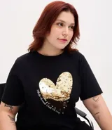 Remera de algodón color negro, con cuello redondo y mangas cortas. Presenta una estampa central en forma de corazón realizada con lentejuelas reversibles en tonos dorados y plateados.