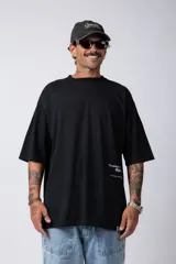 Remera blanca de corte oversize con cuello redondo y mangas cortas. Presenta un pequeño estampado tipográfico en la parte inferior frontal y un diseño gráfico de mayor tamaño en la espalda.