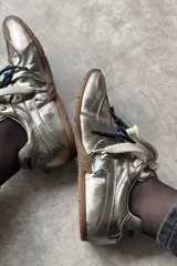Championes deportivos de cuero color dorado metalizado, con suela de goma y cordones anchos en color crudo y azul oscuro.