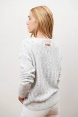 Buzo de punto color gris claro con motas oscuras, escote en V y mangas largas.