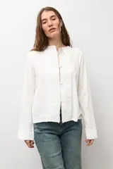 Blusa de manga larga color marrón con cuello redondo y cierre frontal con alamares. Presenta costuras visibles y diseño estructurado.
