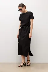 Vestido midi negro de manga corta y cuello redondo, con detalles de botones plateados en el hombro izquierdo, tajo lateral y un cinturón fino ajustable con hebilla metálica.
