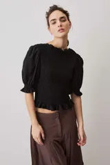Blusa negra con cuerpo fruncido tipo smock, mangas cortas abullonadas con puños elásticos y volados en el cuello y el ruedo.