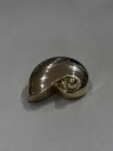 Pin decorativo con forma de caracola en acabado dorado brillante.