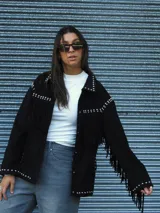 Chaqueta de gamuza negra con flecos en el pecho y mangas, decorada con tachas metálicas en el canesú, cuello y ruedo. Posee cierre frontal y forro interior.