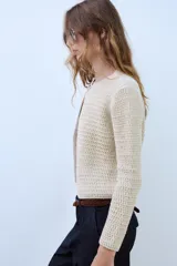Chaqueta de punto de hilo metalizado color beige con cuello redondo, manga larga y cierre frontal con un botón dorado.