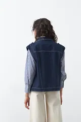 Chaleco de jean en tono celeste claro, con corte recto, cuello camisero, cierre frontal con botones metálicos y costuras visibles.