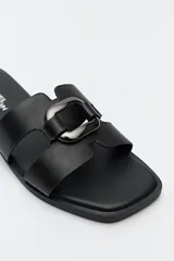 Sandalias planas de diseño abierto, color tostado, con capellada de tiras anchas y un herraje metálico circular en el centro.