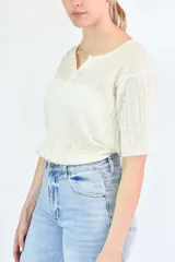 Remera de tejido de punto fino en color crudo, con cuello redondo y pequeña abertura frontal, mangas cortas y textura acanalada.