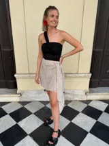 Falda cruzada corta color beige con estampado de lunares negros. Presenta un lazo ajustable en la cintura y un ruedo asimétrico con caída.