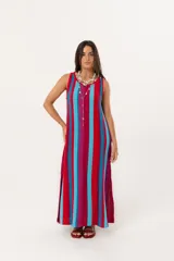 Vestido largo tejido de punto con diseño de rayas verticales en colores vibrantes, escote bote y mangas sisa. Presenta tajos laterales en el ruedo que aportan movimiento.