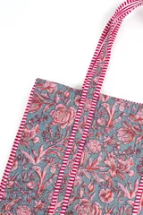 Bolso tipo tote bag acolchado, con estampado floral en tonos rosados y marrones sobre fondo blanco. Posee asas de hombro y ribetes con diseño de rayas rojas y blancas.