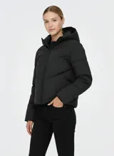 Campera puffer corta, color negro, con capucha fija y cierre frontal de cremallera. Presenta un diseño acolchado con costuras en forma de zigzag y puños internos en las mangas.