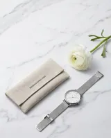 Reloj analógico de mujer con caja redonda plateada, esfera minimalista con índices de puntos y malla de acero tipo milanesa. Diseño elegante y versátil.