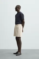 Bermuda de algodón color beige claro, de corte regular fit, con cintura elástica ajustable mediante cordón. Presenta bolsillos laterales y un bolsillo trasero de vivo.